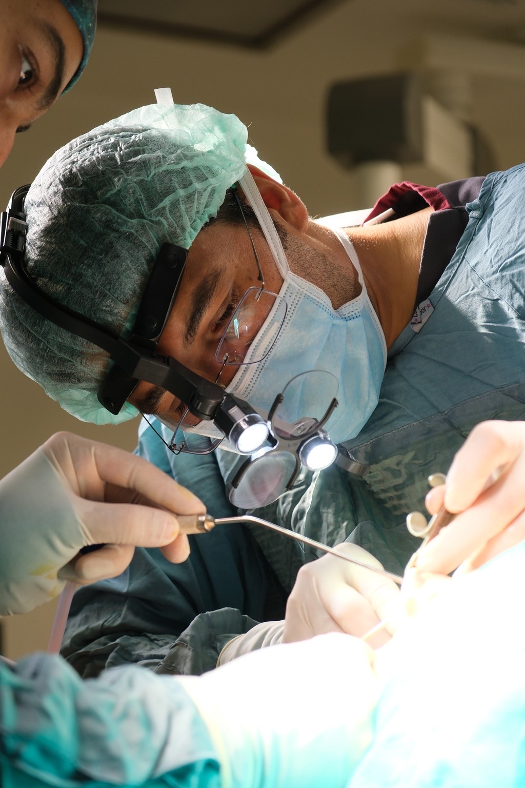 Dr. Cemil Işık performing microsurgery in the operating room, wearing surgical loupes